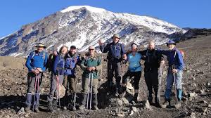 Team of hikers celebrating on a rocky ridge with Kilimanjaro behind